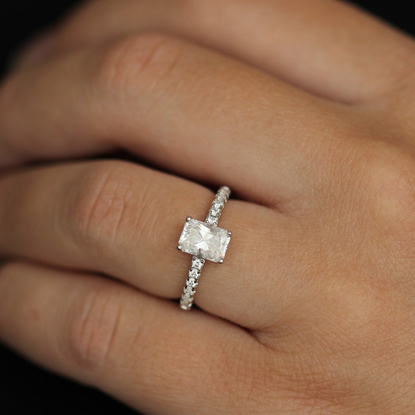 1 carat radiant cut moissanite ring with a pavé set band on model finger