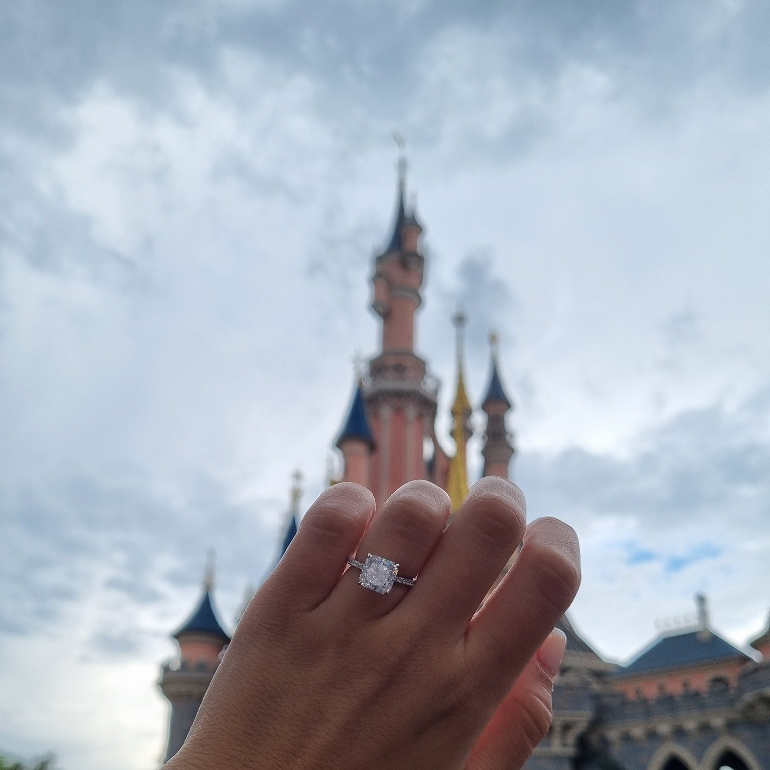 Silver radiant cut ring on hand in front of Disneyland castle Paris