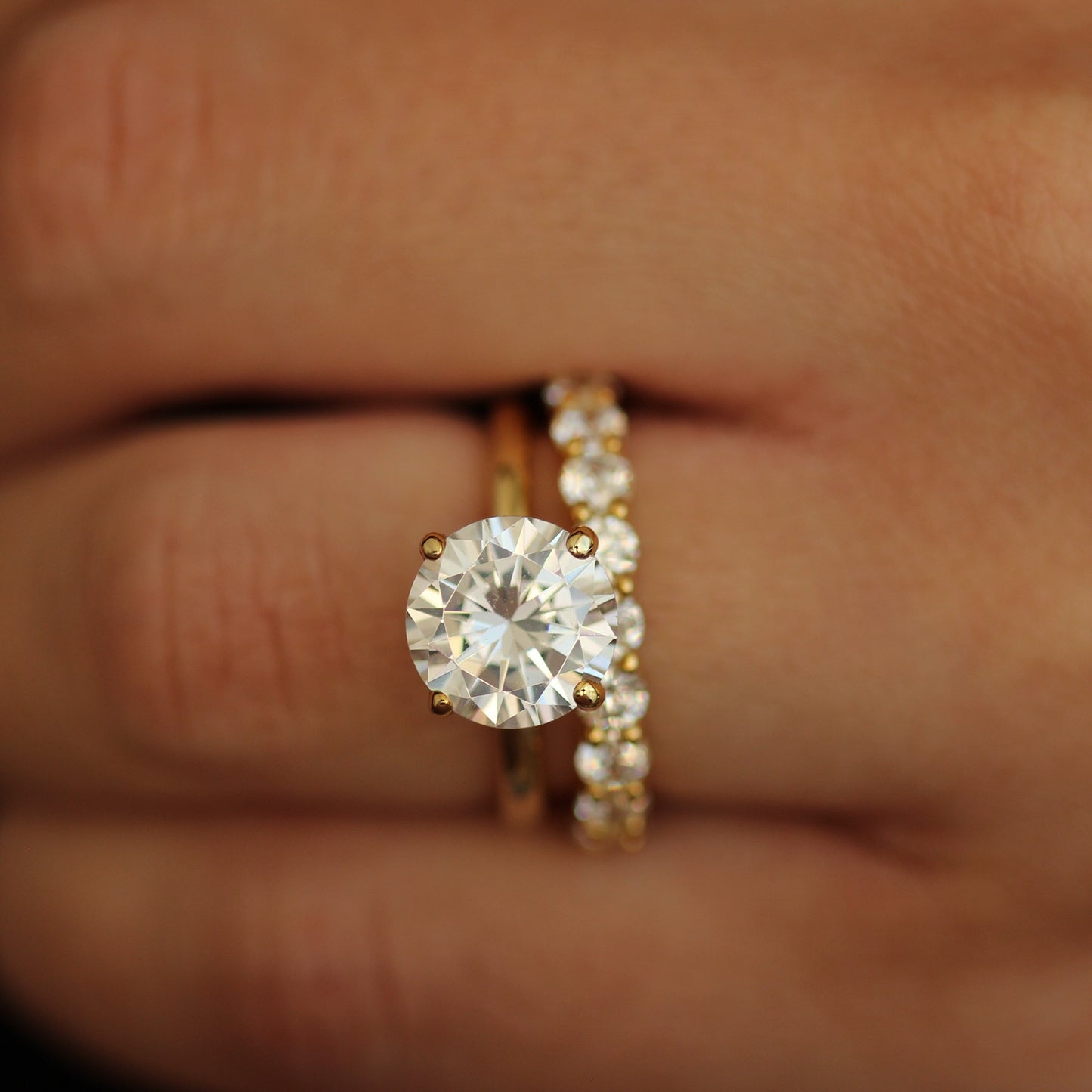 Gold ring with a 3ct round stone on a hand against a dark background