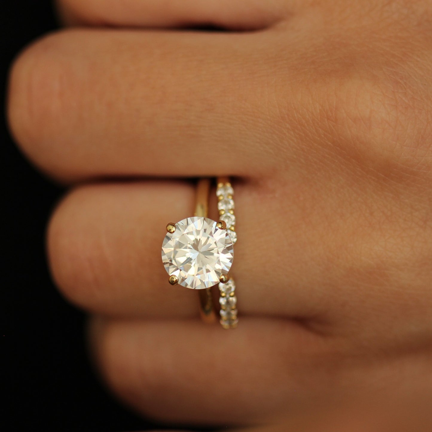 Gold ring with a 3ct round stone on a hand against a dark background