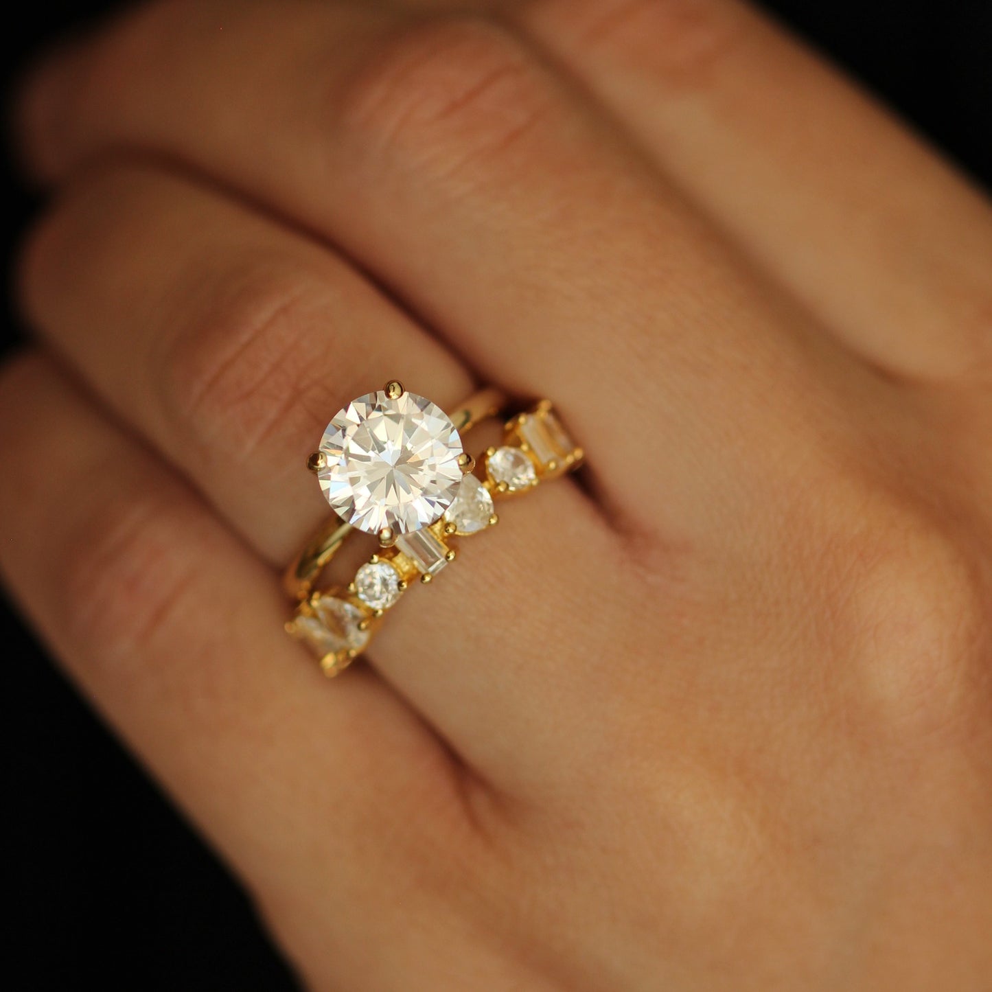 Gold ring with a 3ct round stone with a stacker ring on a hand against a dark background