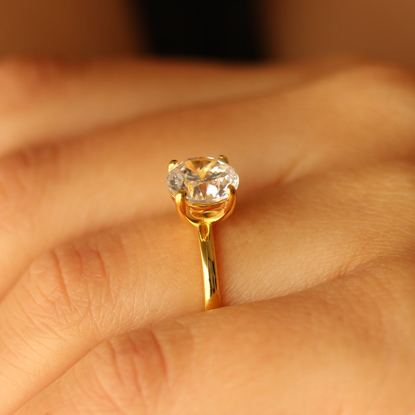 Gold ring with a round gemstone on a finger against a blurred background