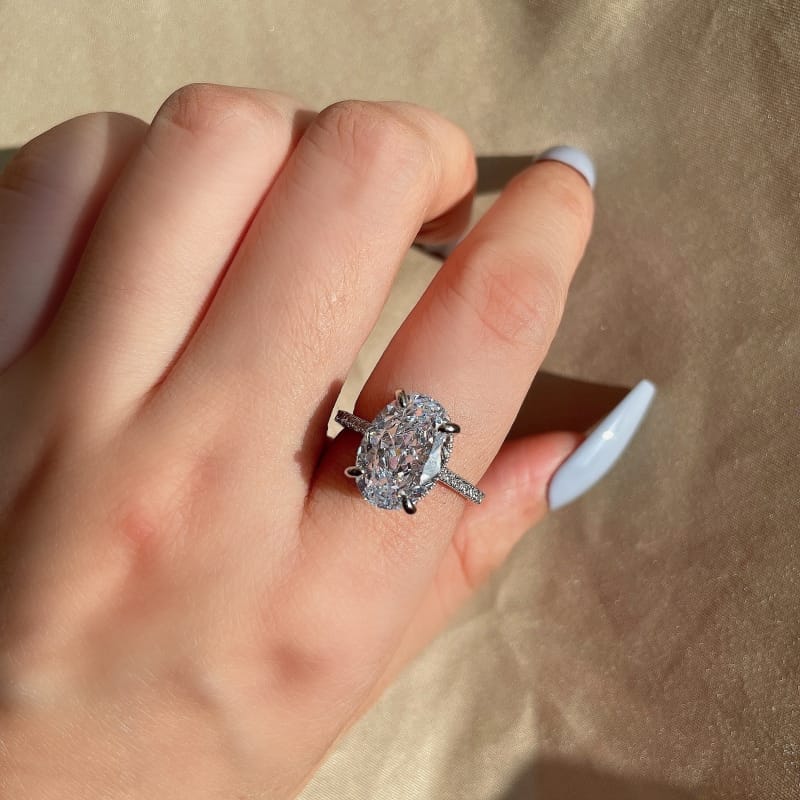 4 carat oval engagement ring with hidden halo in silver on girls hand with light blue nails