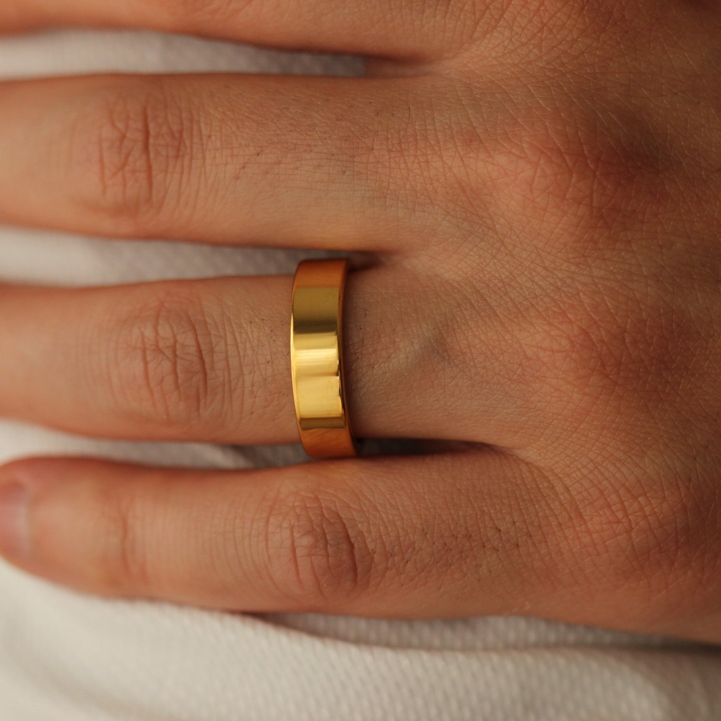 Polished Gold flat wedding band on a person's finger with a neutral background