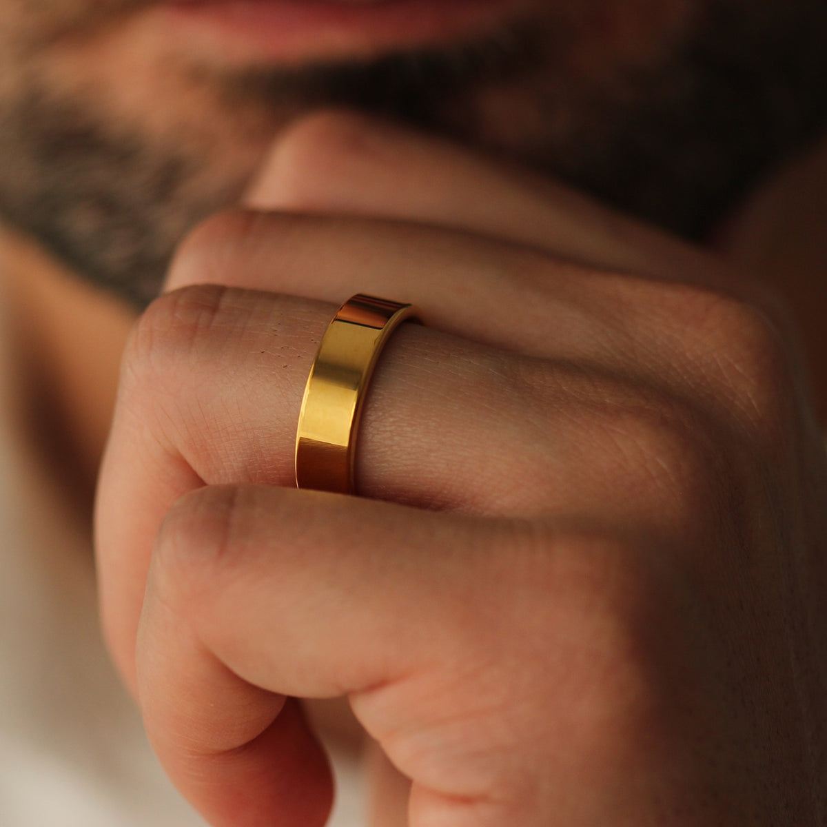Polished Gold flat wedding band on a person's finger with a neutral background