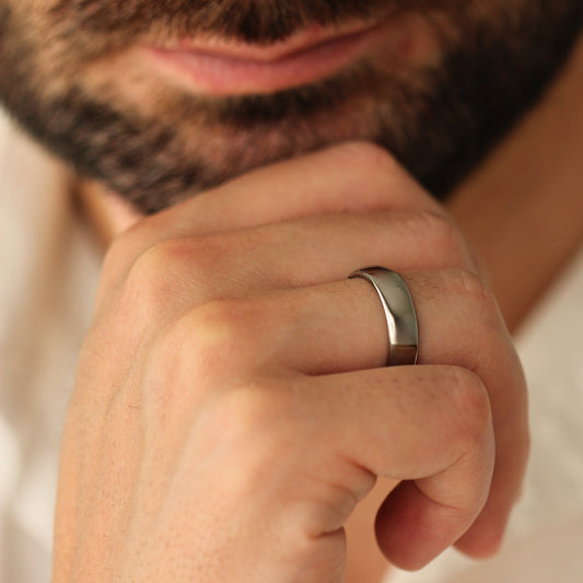 Close-up of a man's hand wearing a polished silver wedding ring with a blurred background