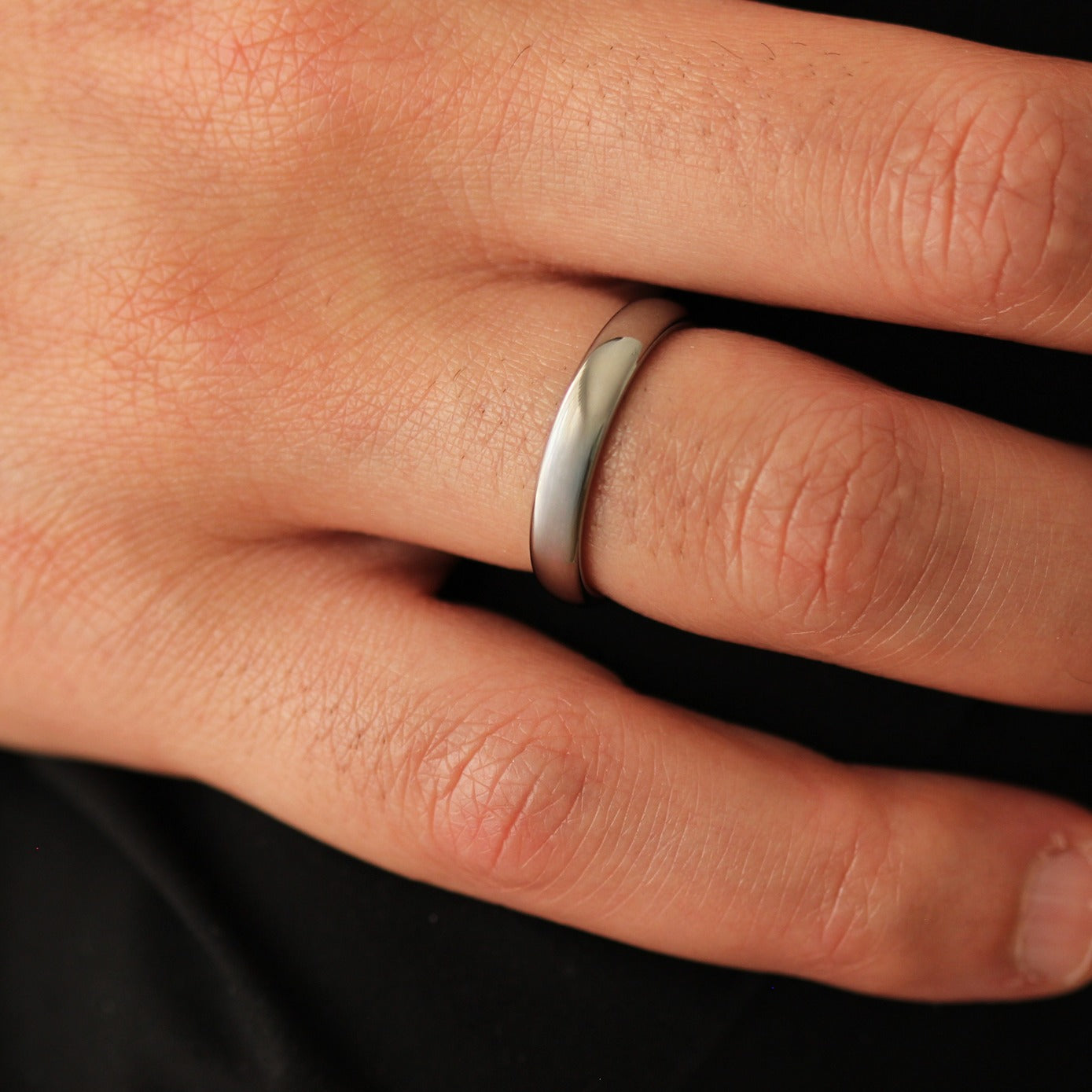 Close-up of a men's hand wearing a polished silver wedding ring on a dark background