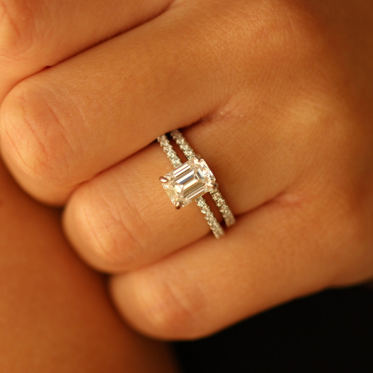 Emerald cut moissanite ring on hand with pave band