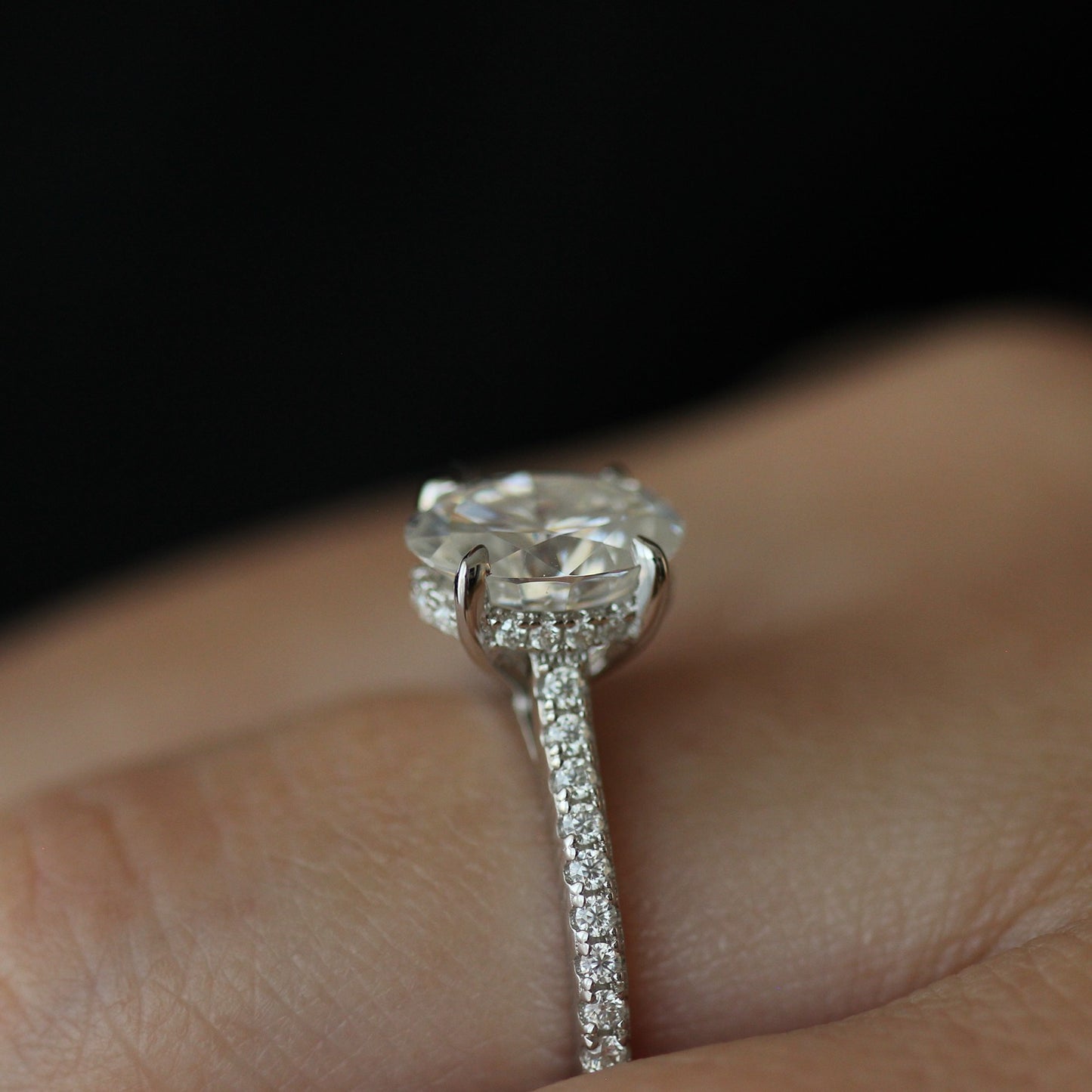 Side view of 2ct oval moissanite ring with pave band on hand