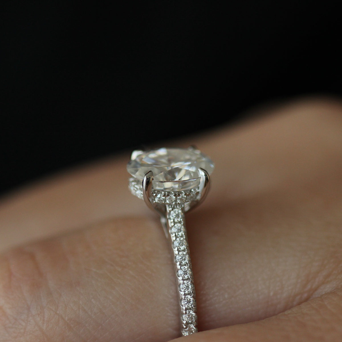 Side view of 2ct oval moissanite ring with pave band on hand