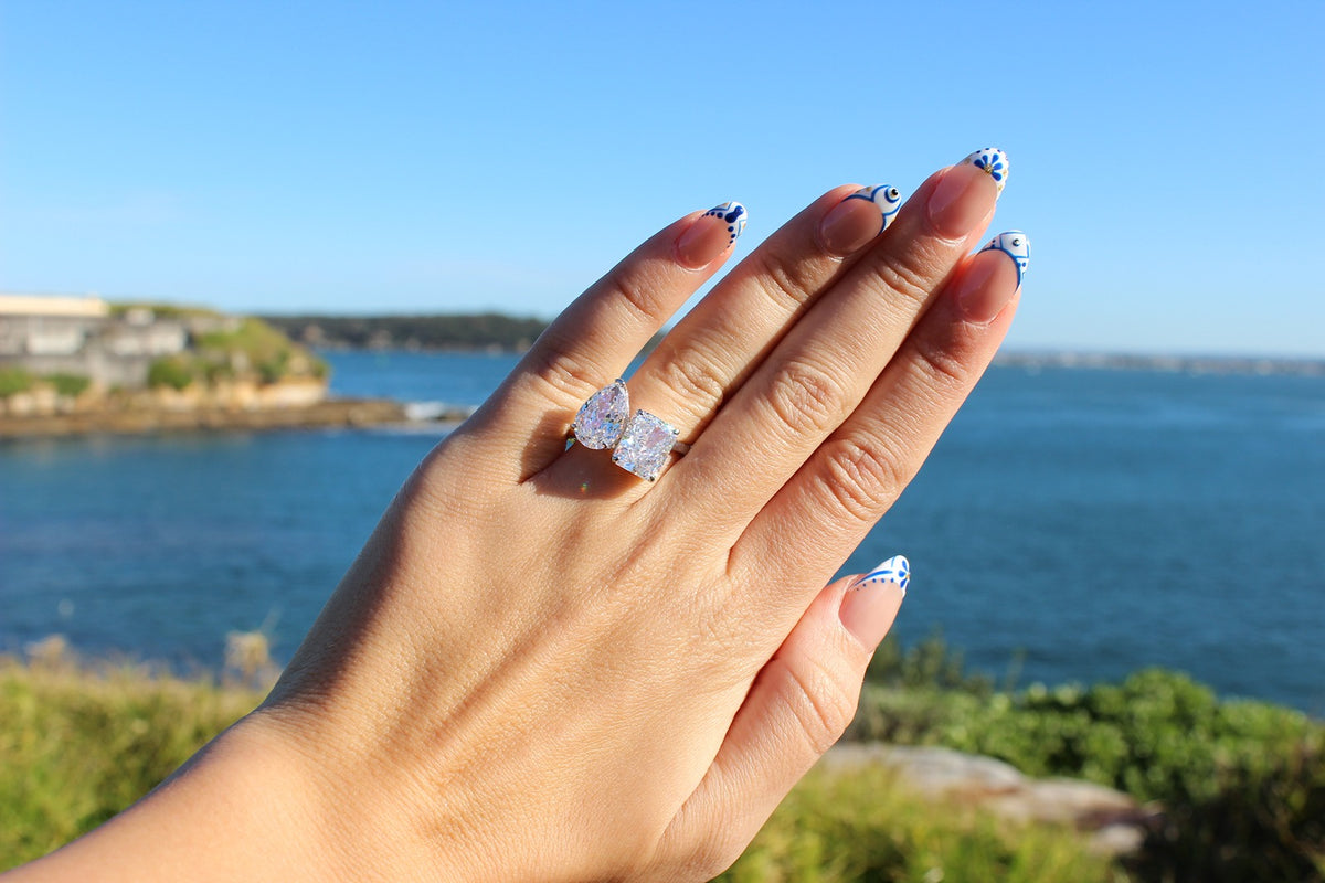 silver toi et moi ring with pear and rectangle stone with beach in background