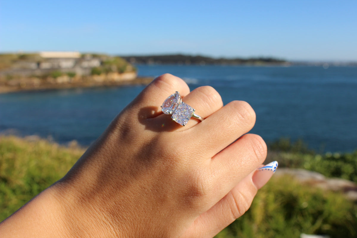 silver toi et moi ring with pear and rectangle stone with beach in background