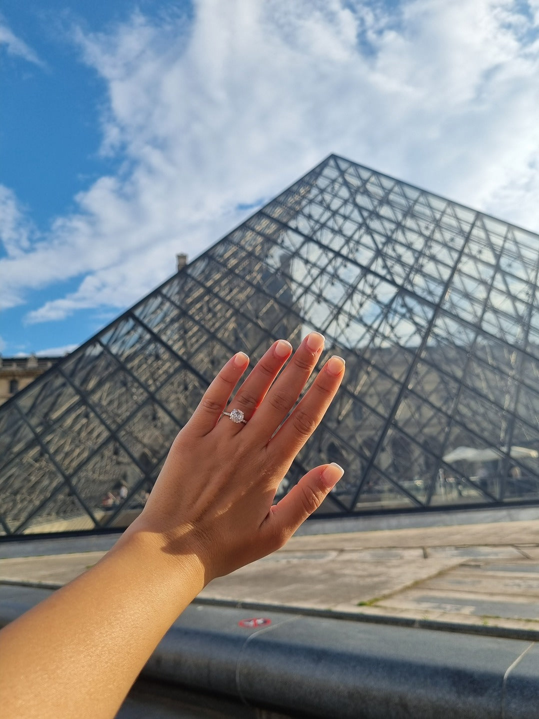 person in front of the louvre musuem showing their round engagement ring