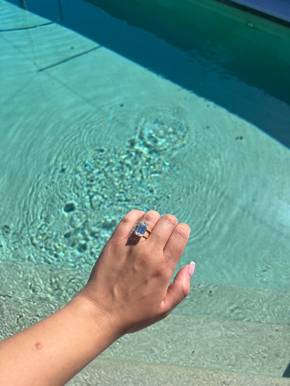 Gold emerald ring with two bands with a pool in the background