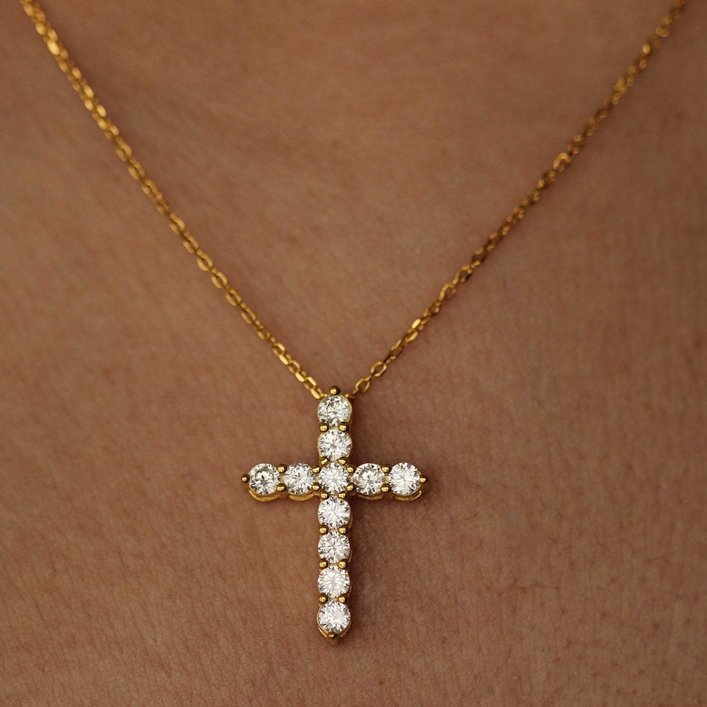 Gold cross necklace with cubic zirconia stones on a person's neck