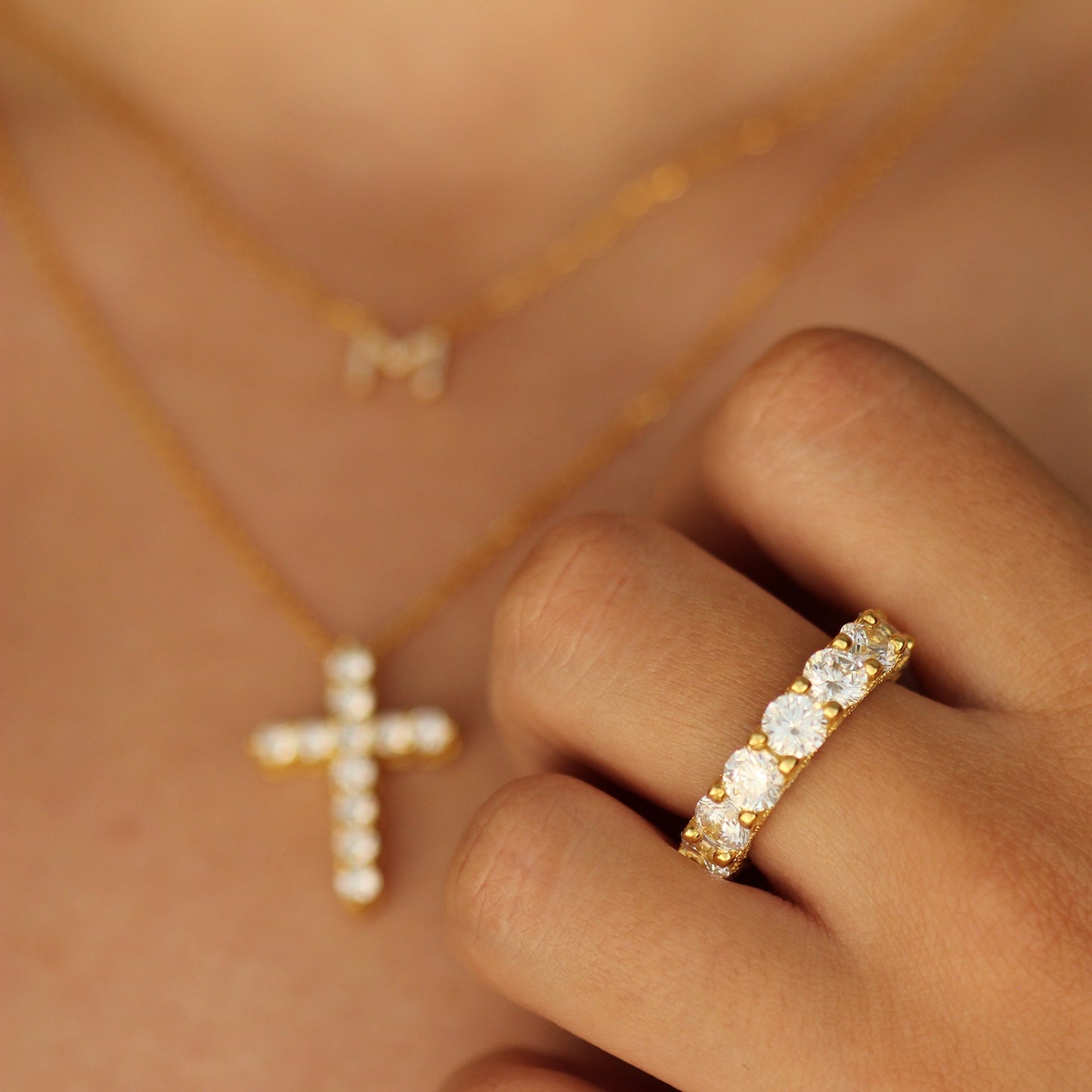 18k plated gold cross necklace and m initial necklace on model with gold stacker ring on hand
