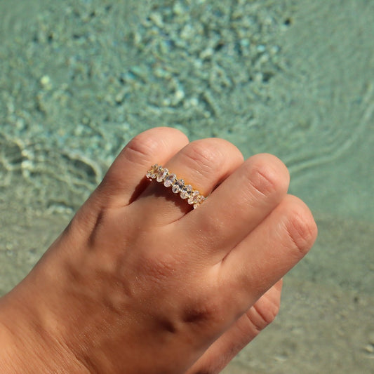 Gold oval stacker ring on hand in front of pool water