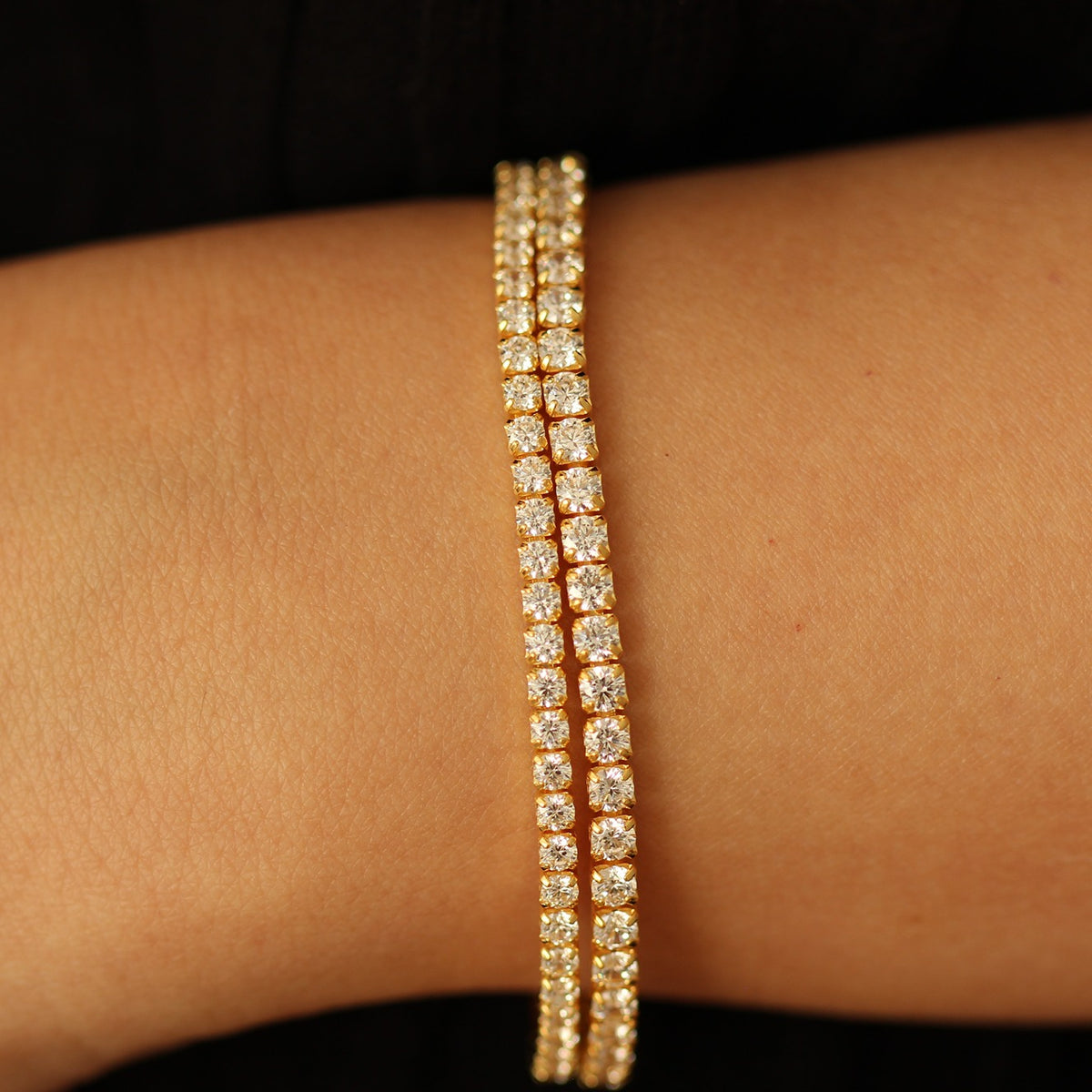3mm Gold tennis bracelet with clear stones on a wrist against a dark background
