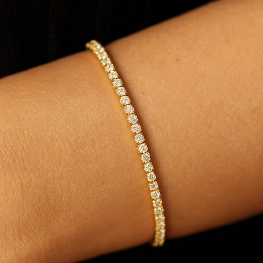 Gold tennis bracelet on a wrist against a dark background