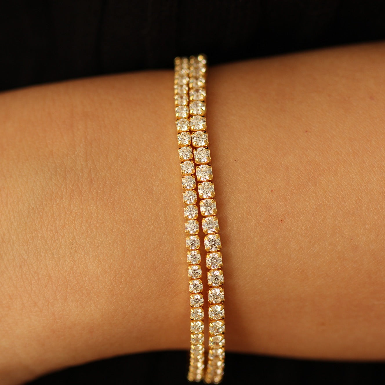 Gold tennis bracelets on a wrist against a dark background