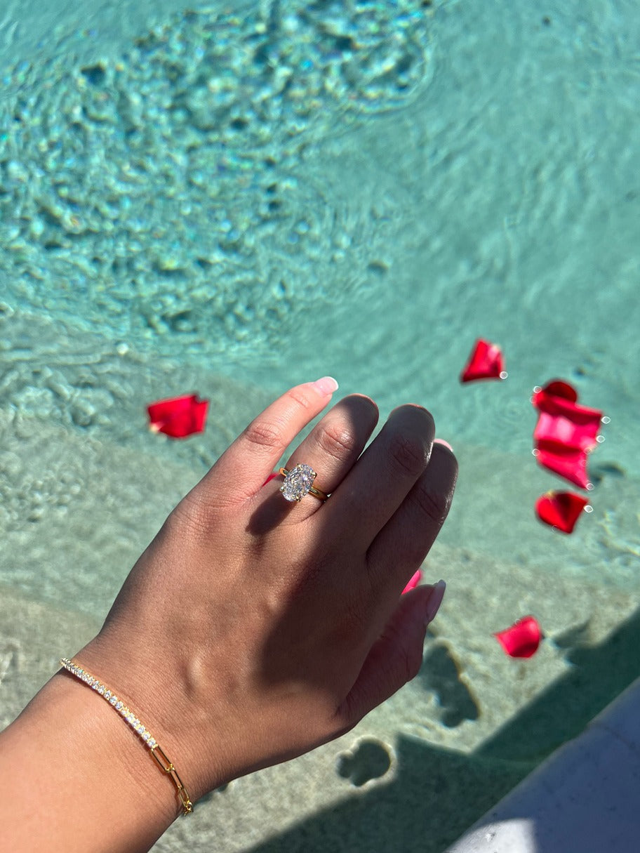 gold tennis chain bracelet being worn with a gold oval ring near a pool