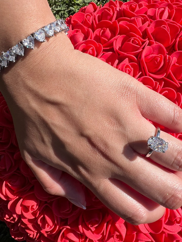 silver oval ring with flower pillow in background and heart shaped bracelet
