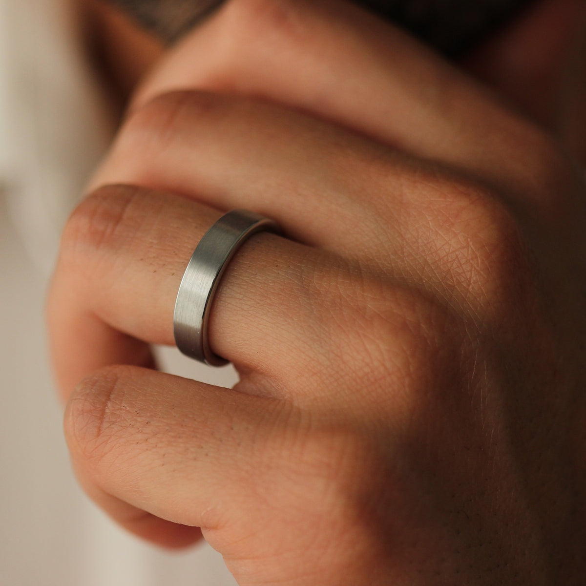 Close-up of a man's hand wearing a brushed silver ring with a blurred background