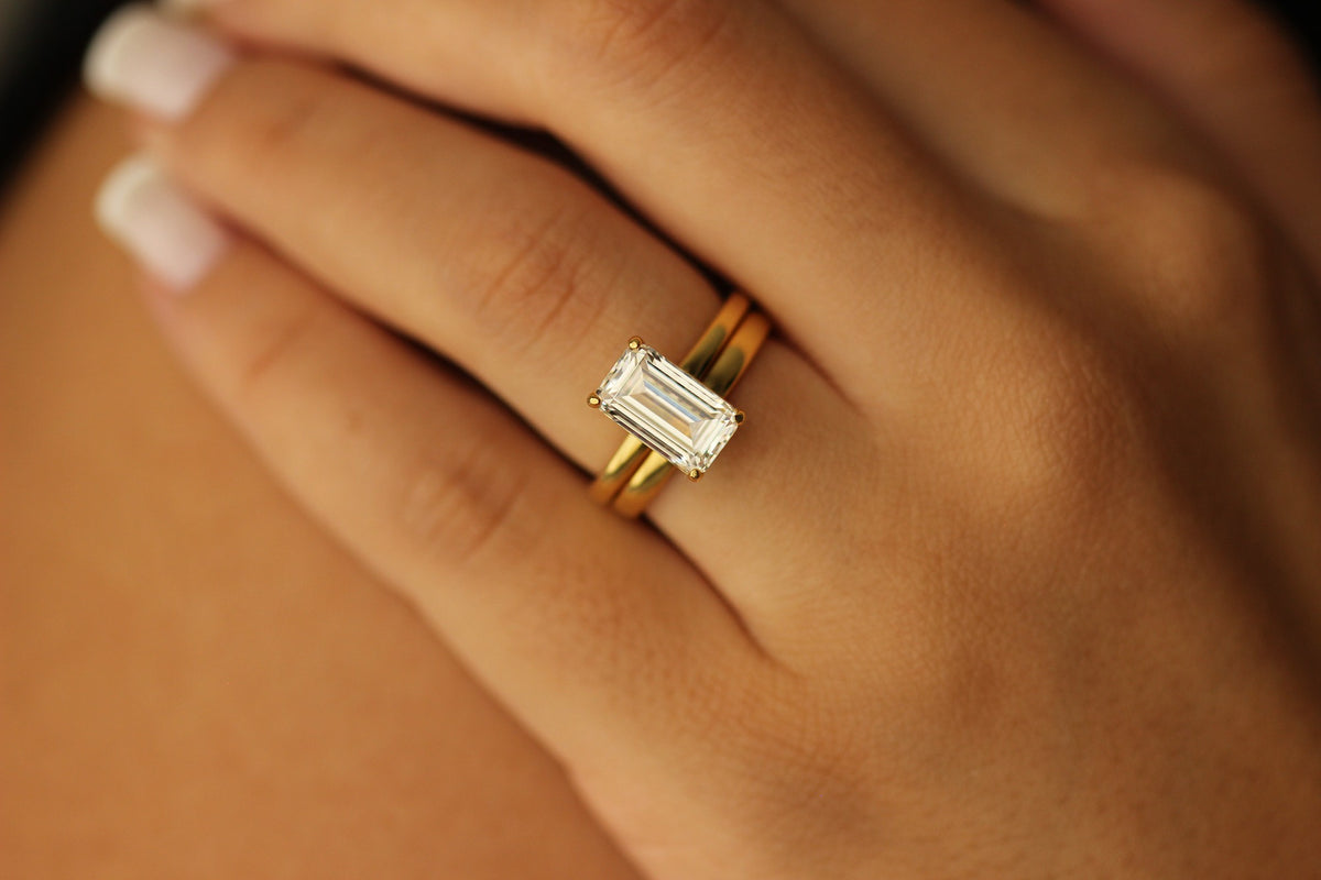 plain gold ring with emerald centre stone on hand and plain 18k gold wedding band