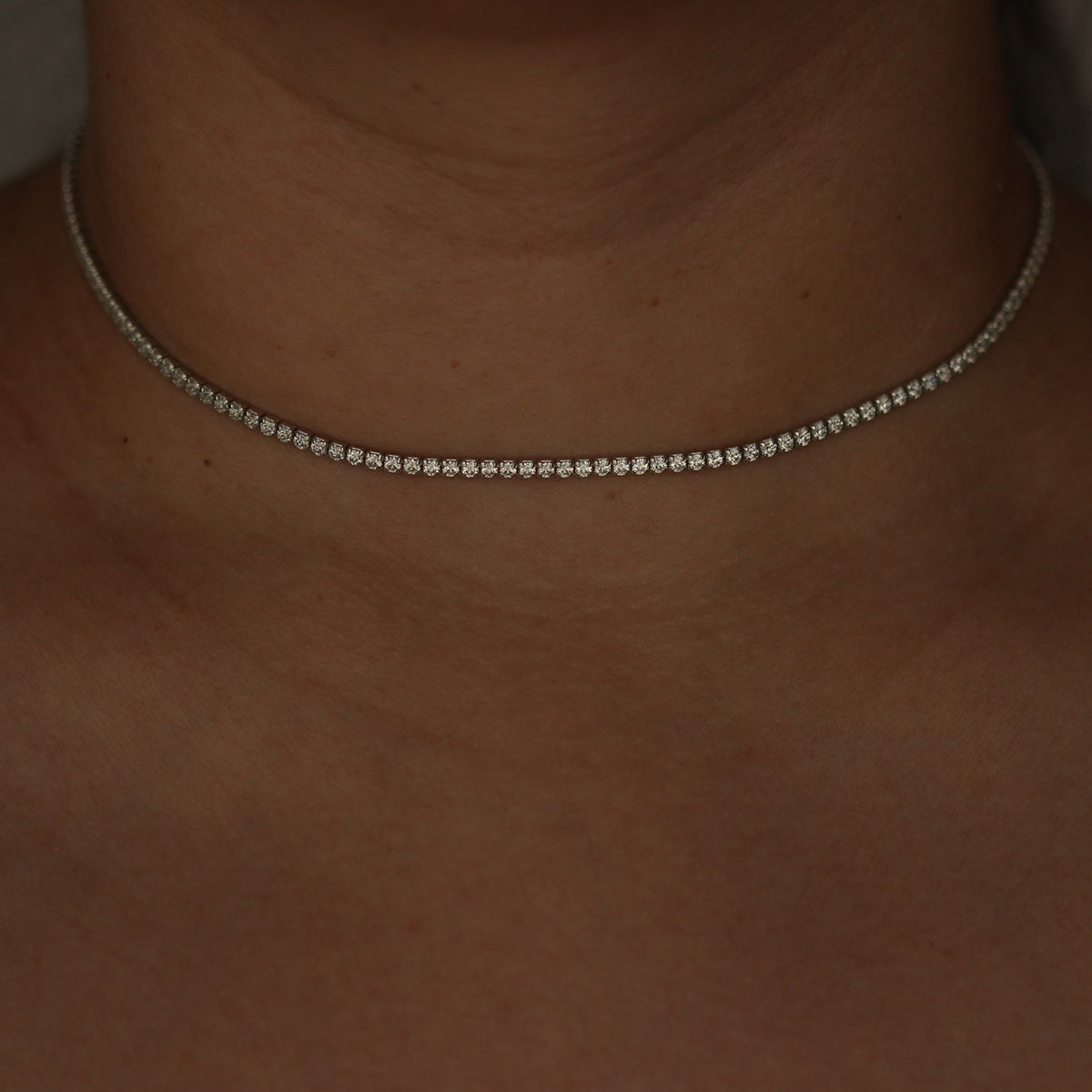 Silver tennis necklace on a person's neck with a blurred background