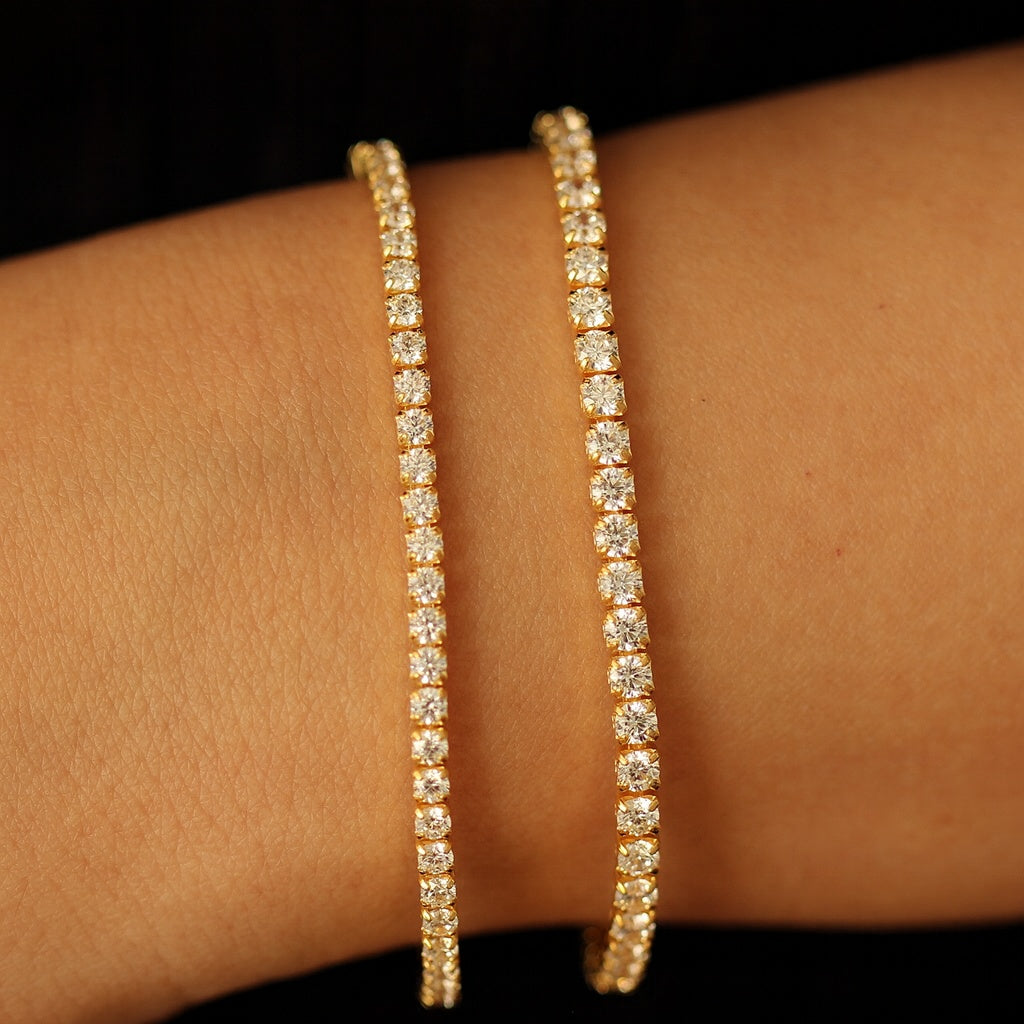 Gold tennis bracelets on a wrist against a dark background