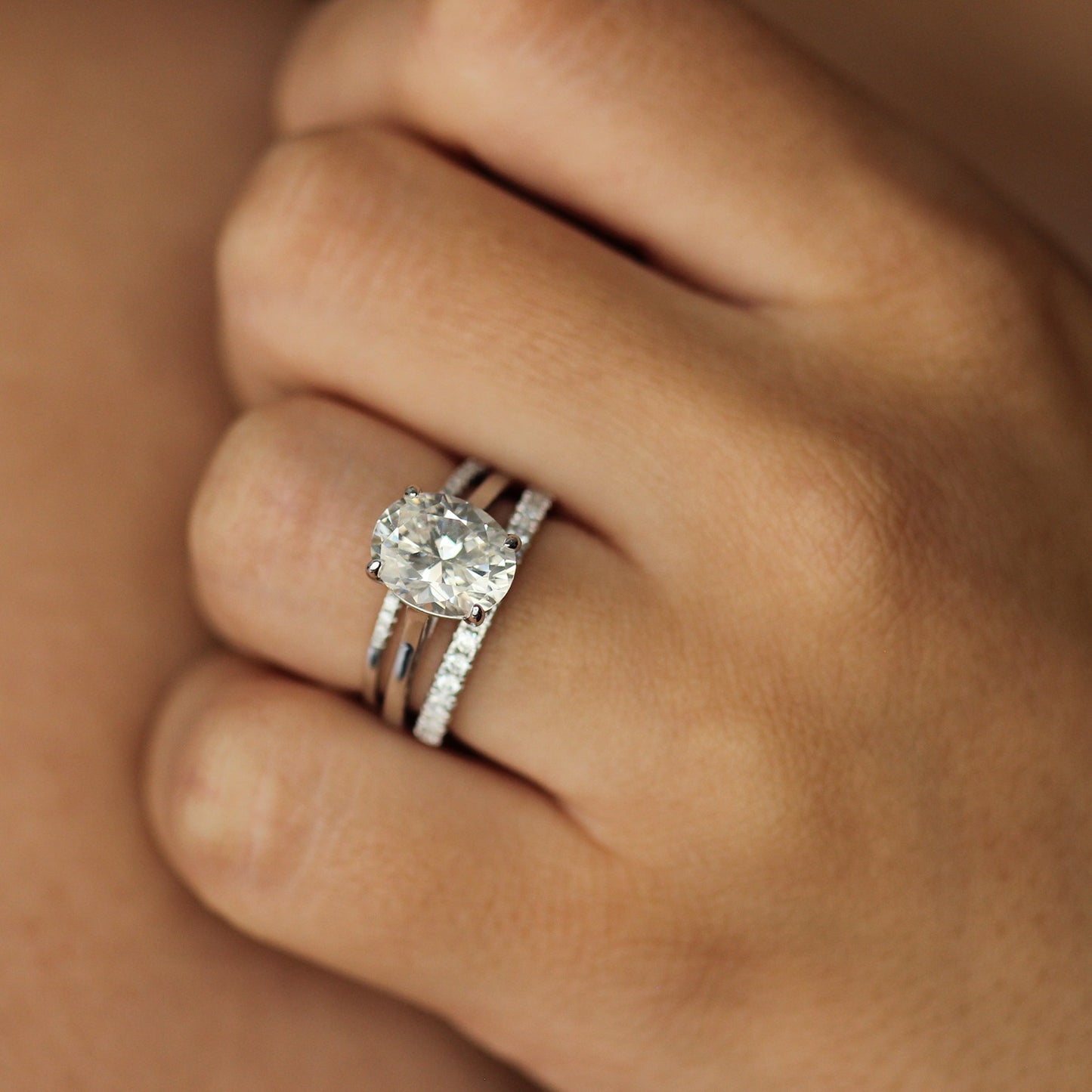 Silver cubic zirconia oval ring on hand with stacker pave rings