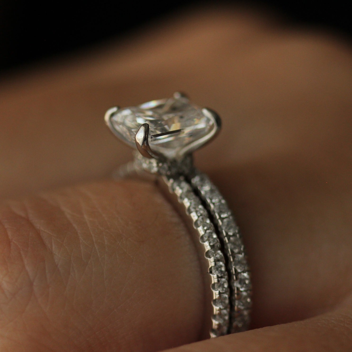 Side profile of radiant cut ring on hand with eternity pave band