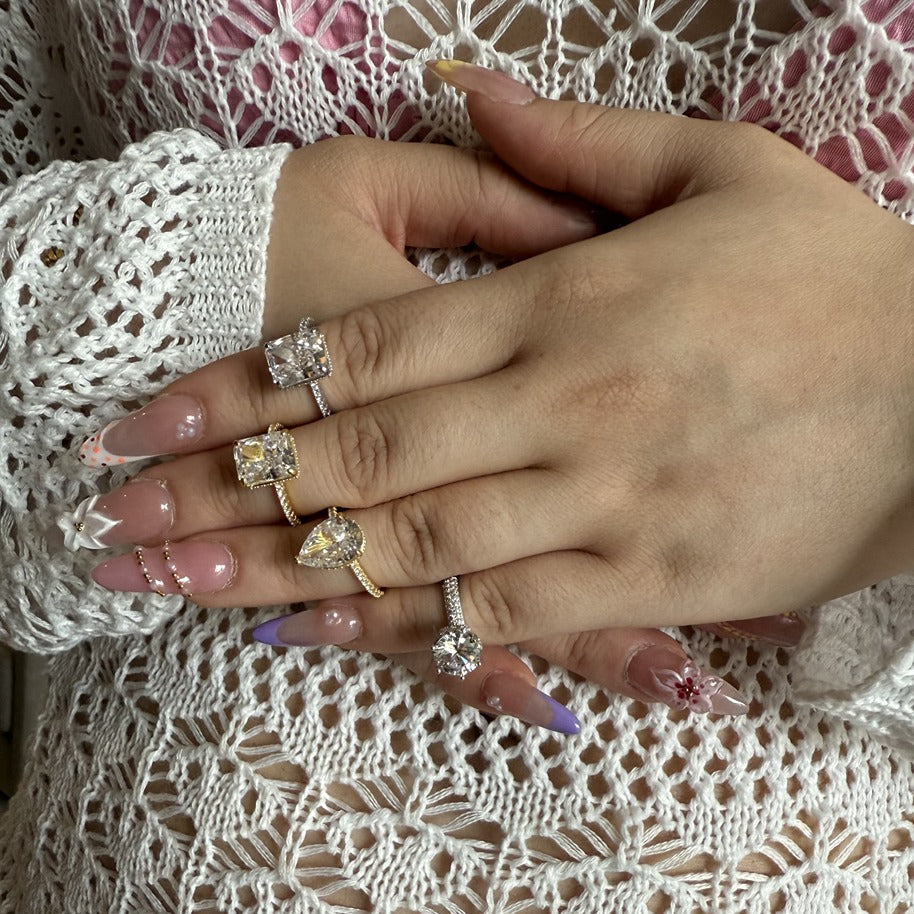 Hand wearing multiple cubic zirconia rings on a textured white fabric background