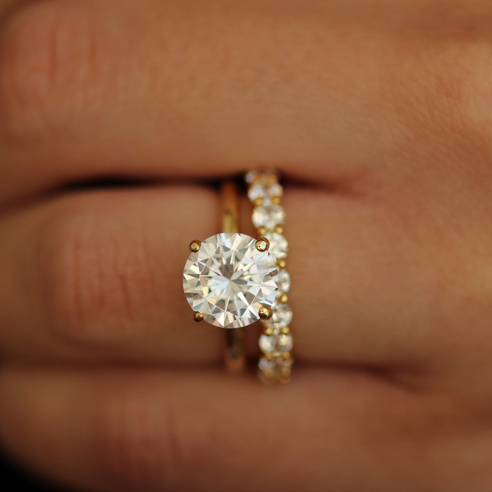 Gold ring with a 3ct round stone on a hand against a dark background