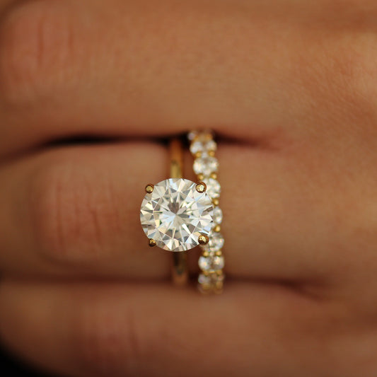 Gold ring with a 3ct round stone on a hand against a dark background