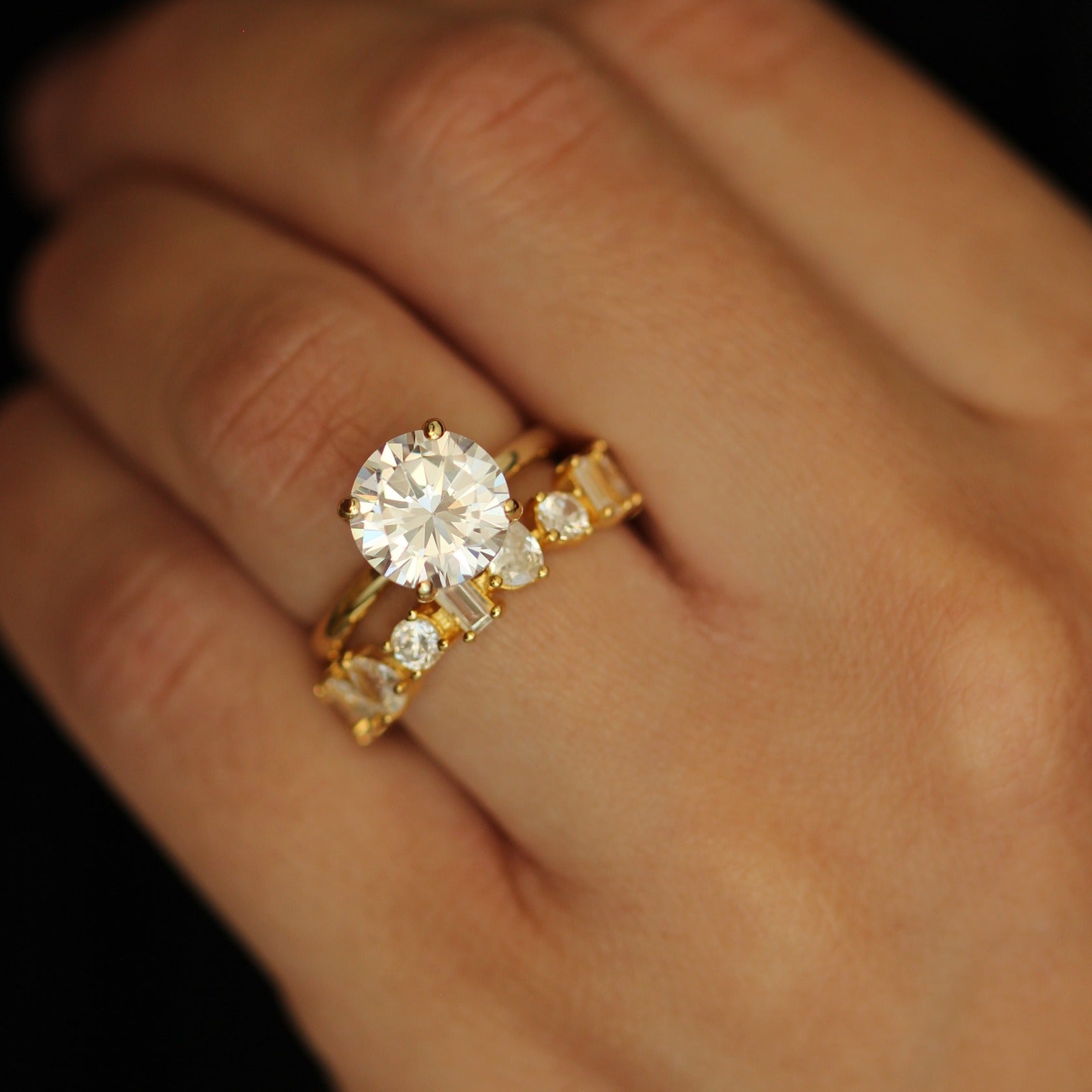 Gold ring with a 3ct round stone with a stacker ring on a hand against a dark background