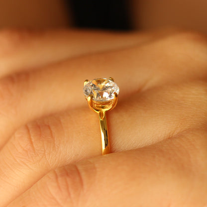 Gold ring with a round gemstone on a finger against a blurred background