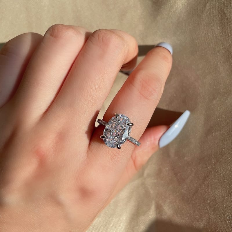 oval ring with hidden halo in silver on girls hand with light blue nails