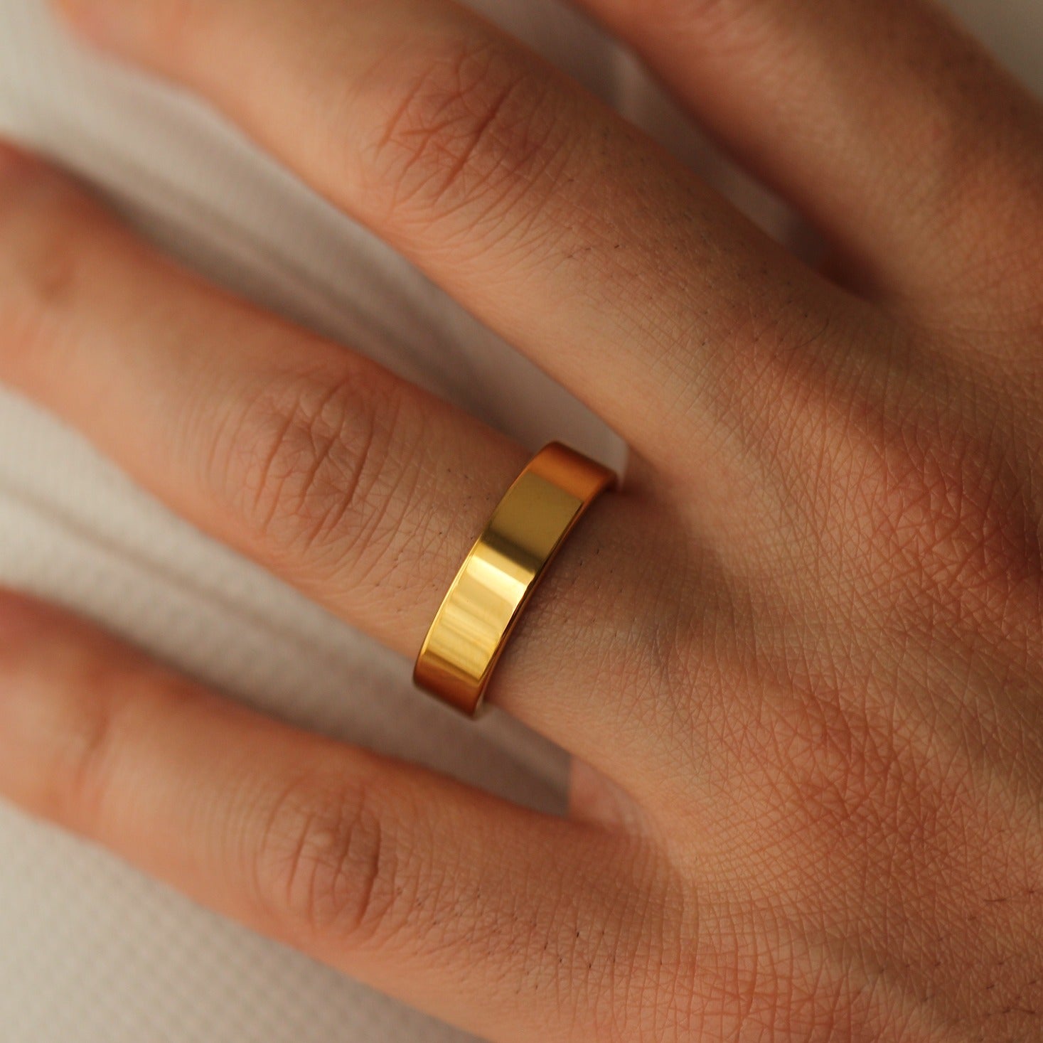 Polished Gold flat wedding band on a person's finger with a neutral background