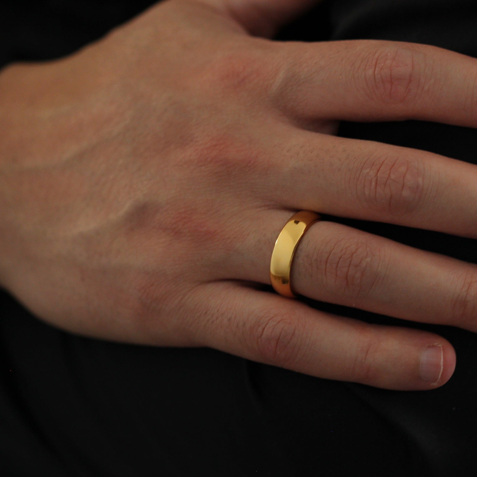 Polished gold wedding ring on a person's finger against a dark background