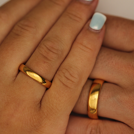 Close-up of two hands wearing two polished gold wedding bands with a blurred background