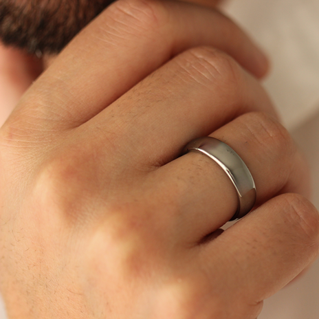 Close-up of a man's hand wearing a polished silver wedding ring with a blurred background