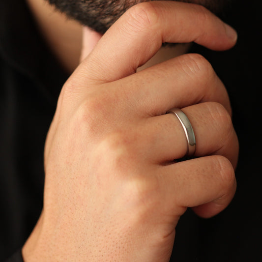 Men's hand wearing a polished silver wedding ring on a dark background