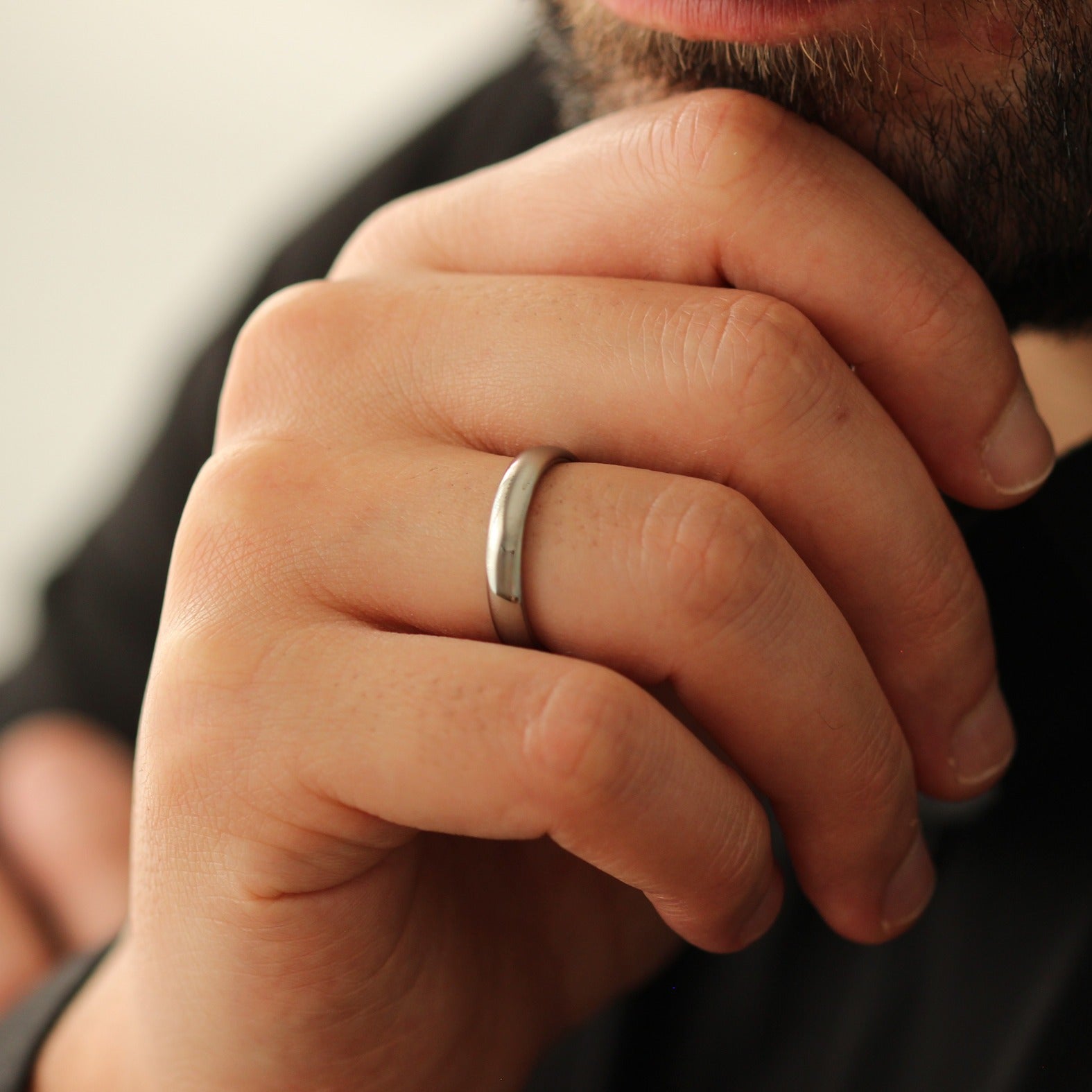 Close-up of a men's hand wearing a polished silver wedding ring with a blurred background