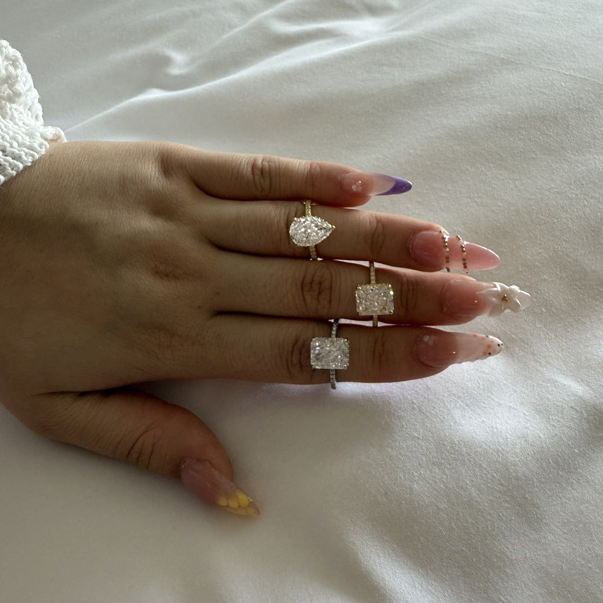 Hand wearing multiple cubic zirconia rings on a white surface