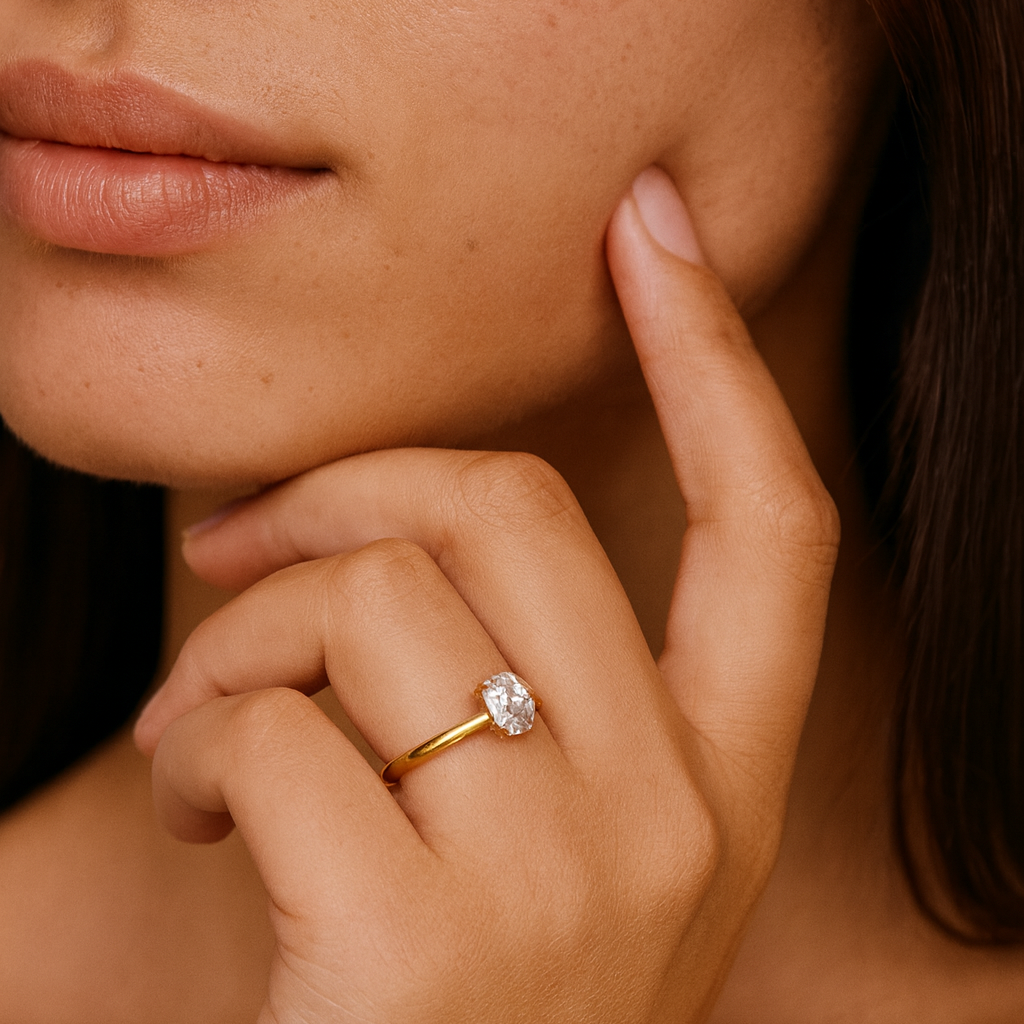 Close up of a hand with 1ct oval gold ring featuring a diamond, touching the cheek