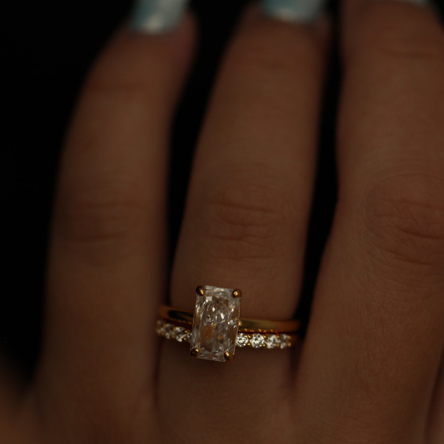 Rectangle Gold ring and gold open band on a person's finger against a dark background