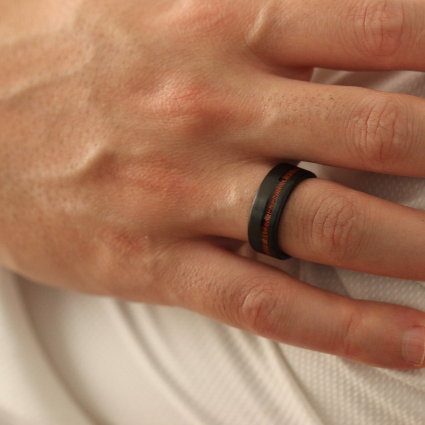 Hand over shoulder wearing a black ring with red wood inlay