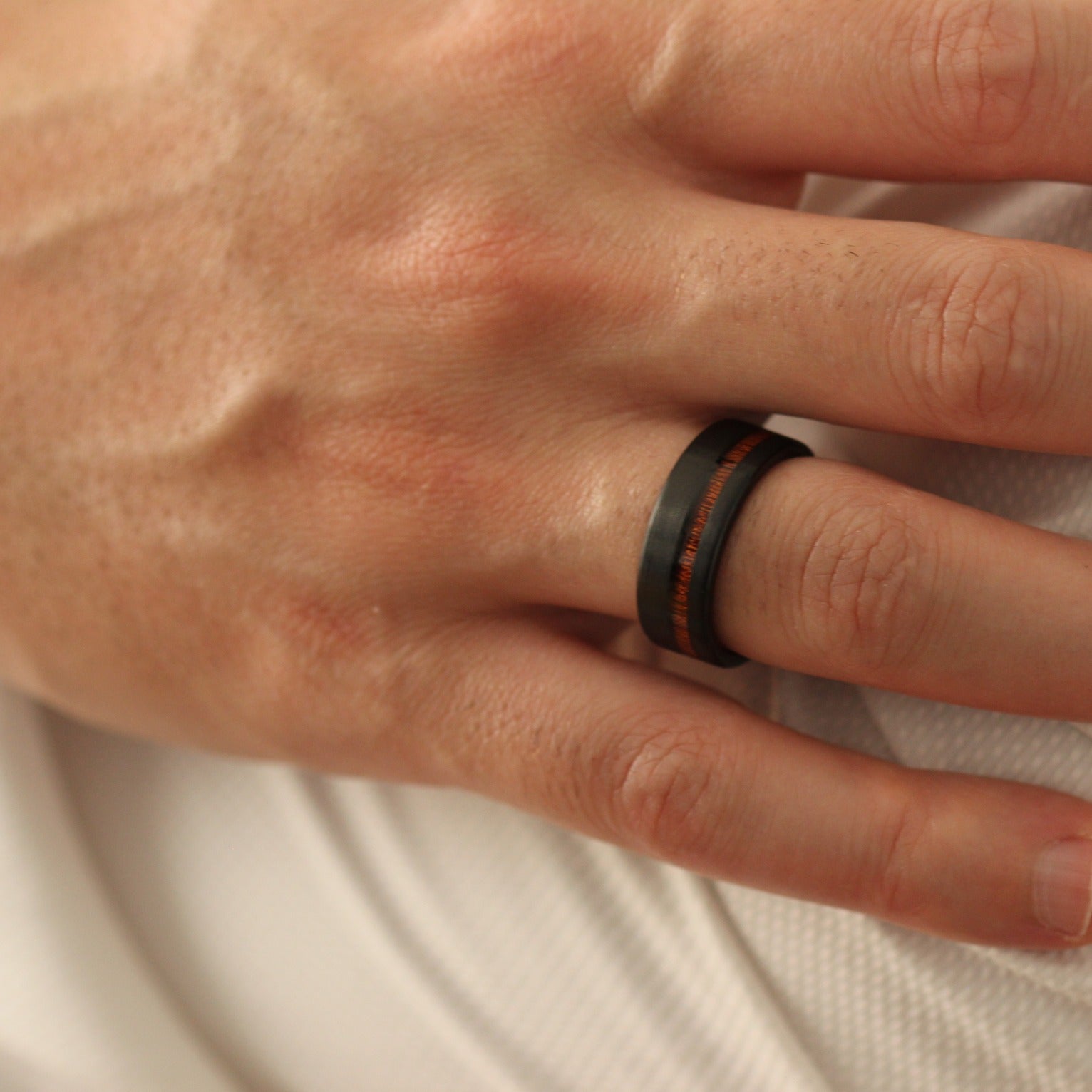 Hand over shoulder wearing a black ring with red wood inlay