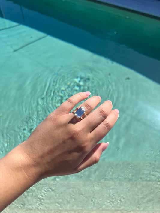 Gold emerald ring with two bands with a pool in the background